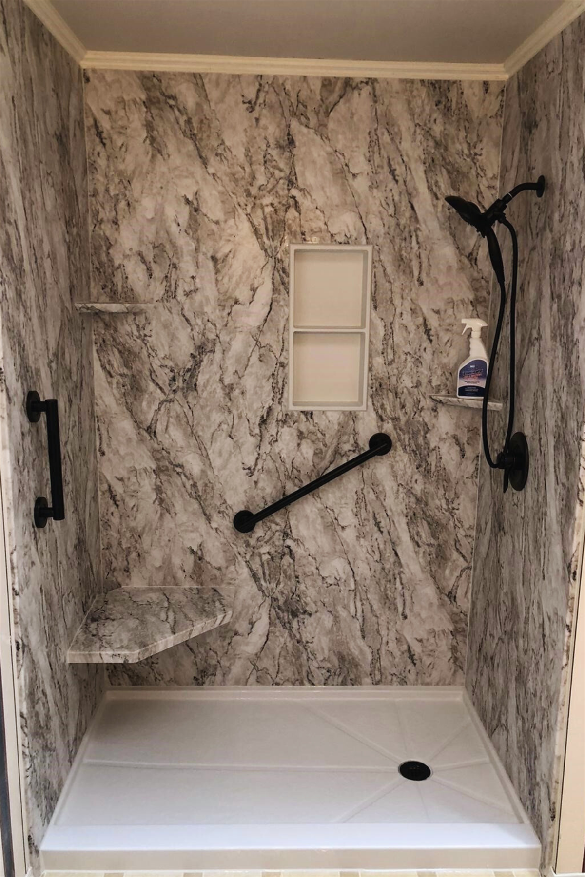 Accessible shower with marble-look walls and black safety grab bars