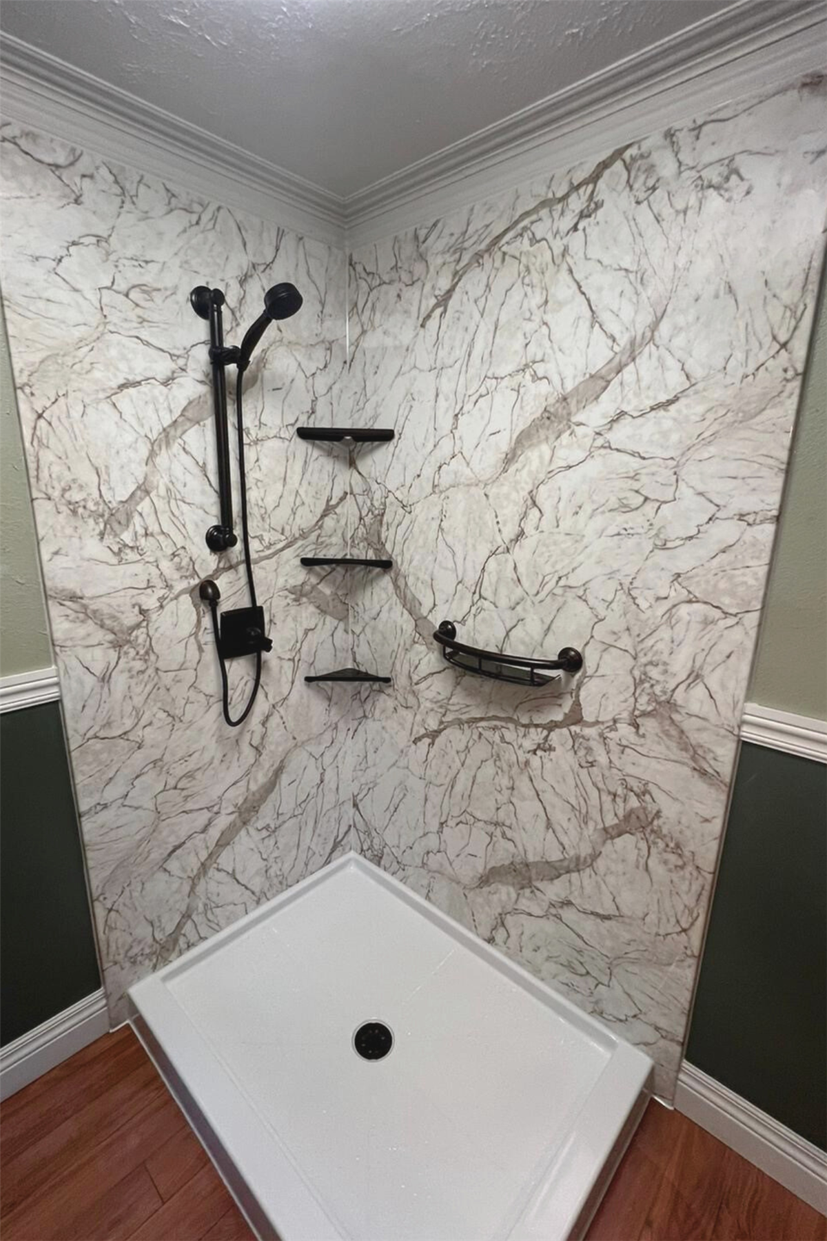 Accessible shower with marble-look walls, black fixtures, storage shelves, and grab bar