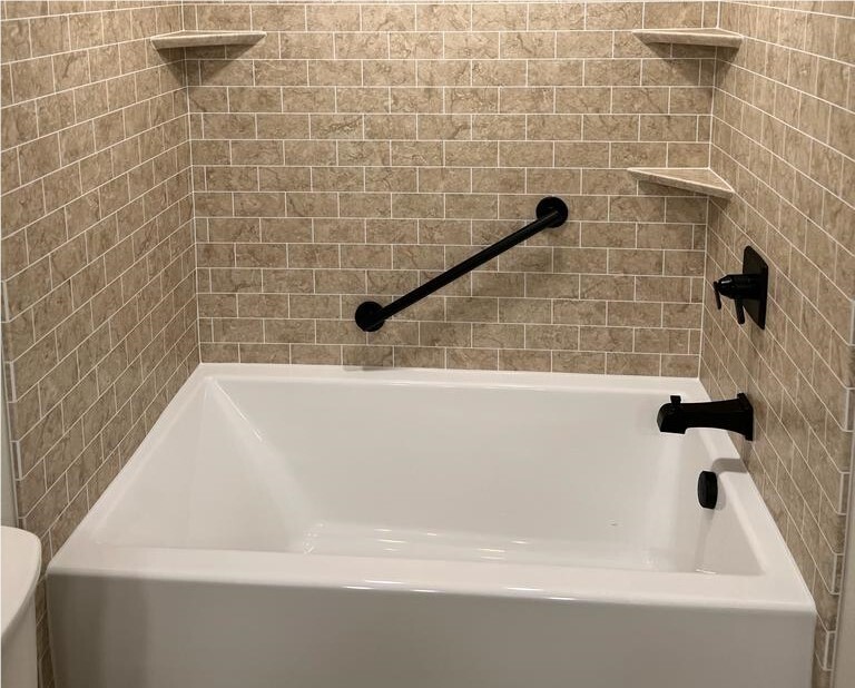 Bathtub with beige tile-look wall surround and black safety grab bar