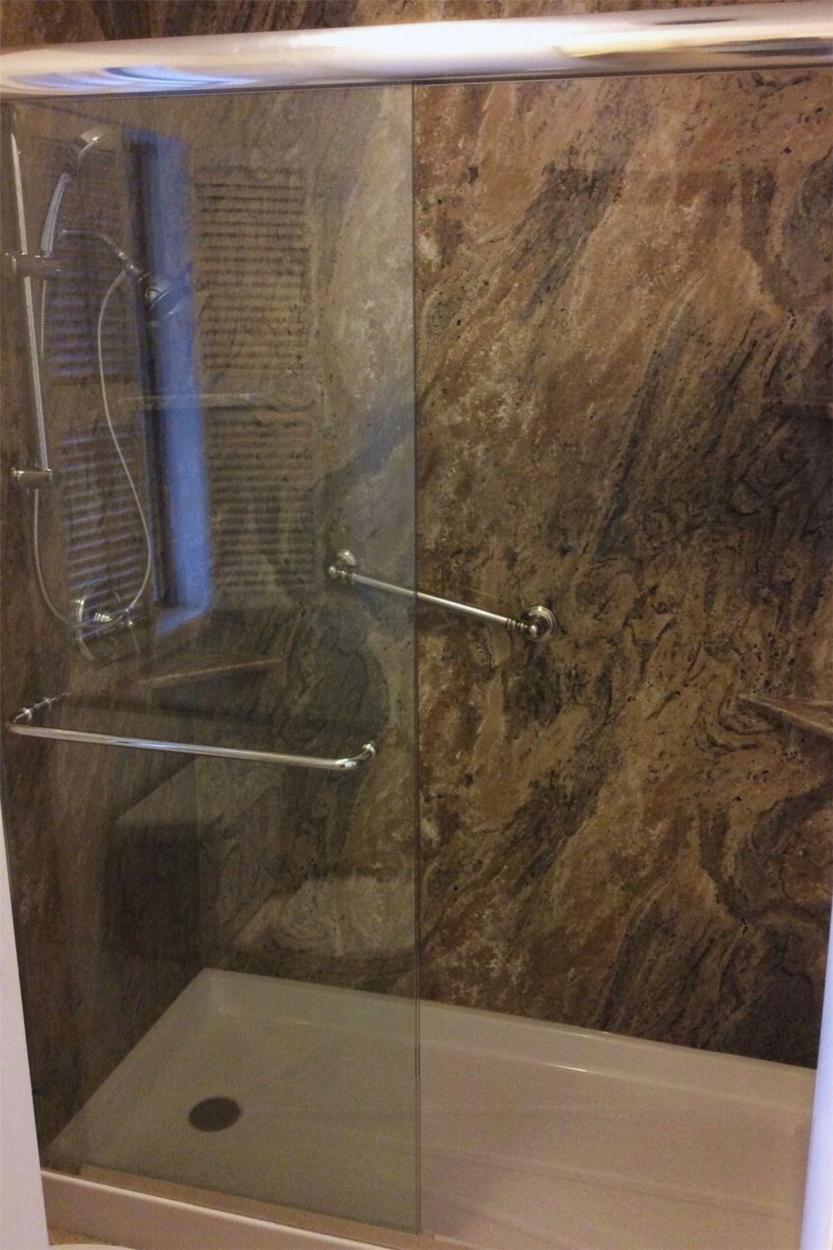 Dark stone-look walk-in shower with glass enclosure and safety grab bar