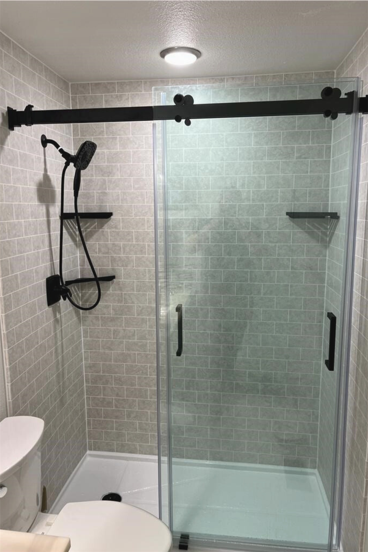 Glass-enclosed shower remodel with gray tile-look walls and black fixtures