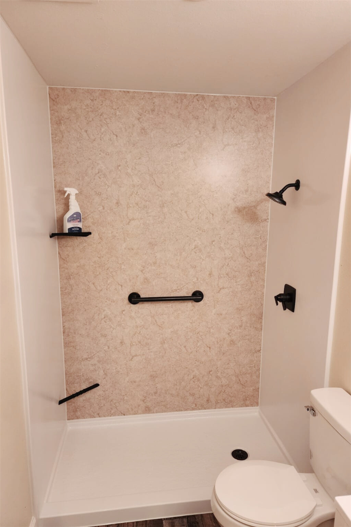 Light stone-look shower wall with black horizontal grab bar