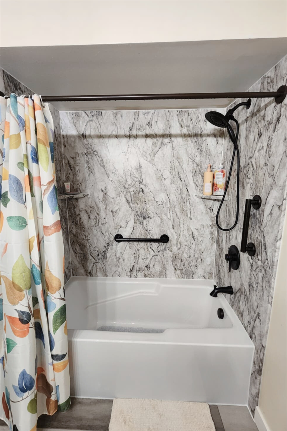 Marble-look bath wall surround with black grab bar and corner storage shelves