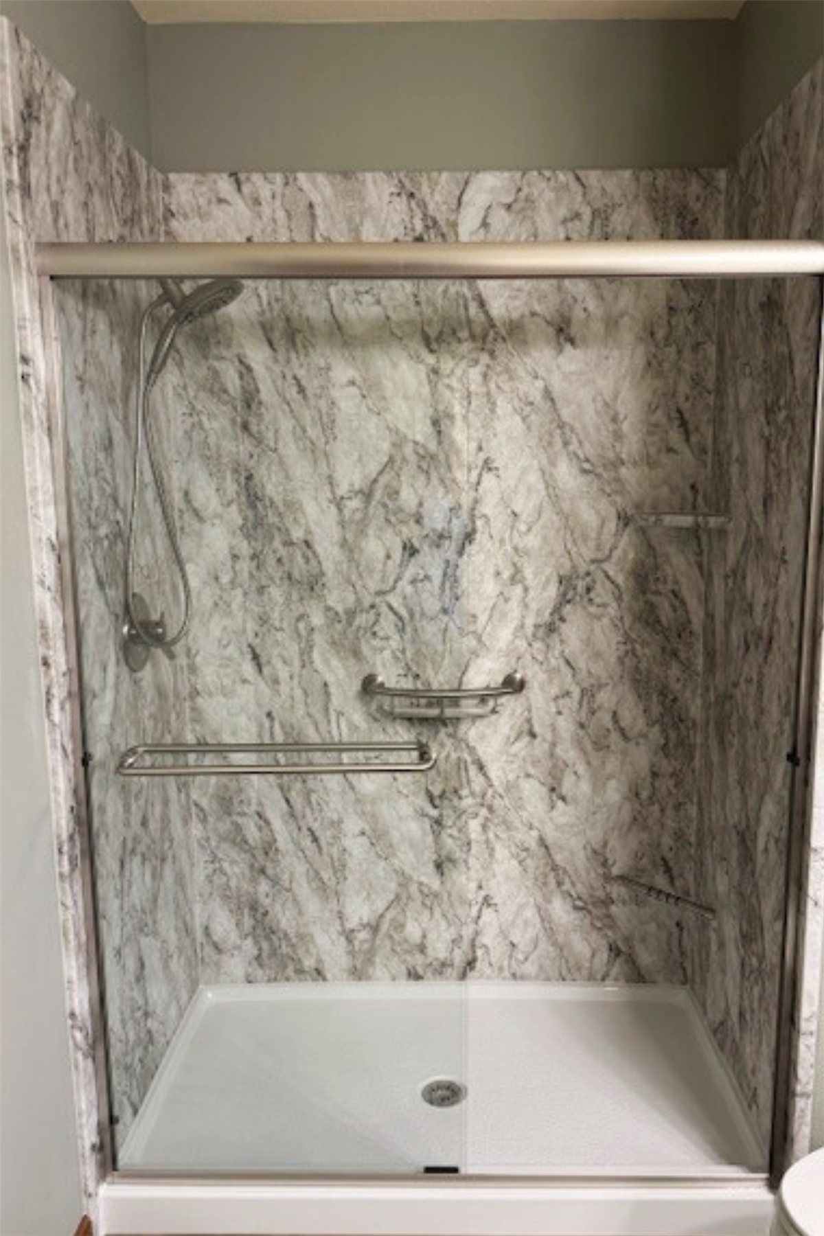 Marble-look walk-in shower with stainless steel grab bars and built-in shelf