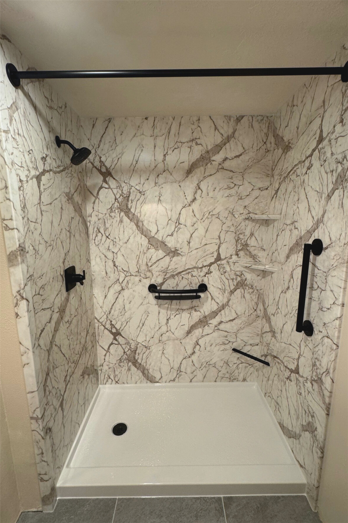 New shower with beige marble-look walls and black safety grab bar