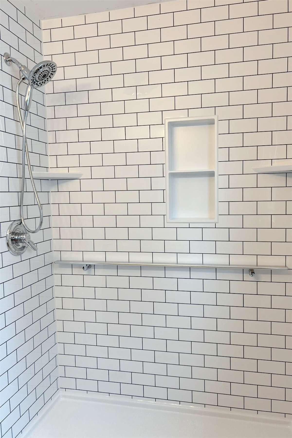 New shower with white subway tile walls and recessed storage niche