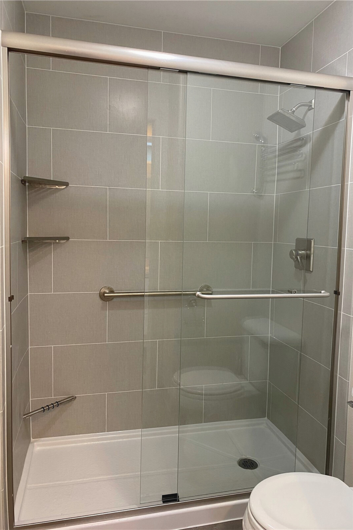 Remodeled shower with gray wall panels and horizontal stainless steel grab bars