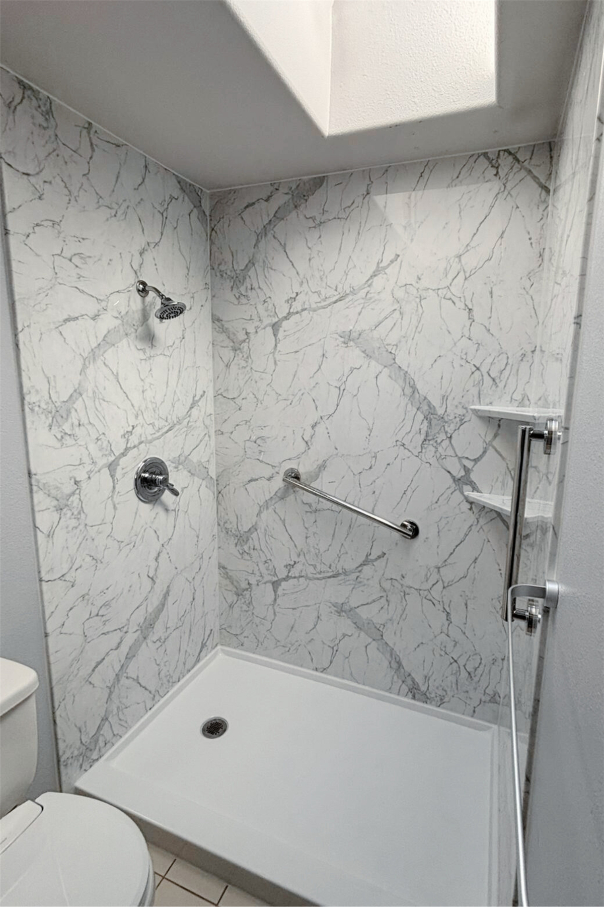 Remodeled shower with white marble-look walls and stainless steel safety grab bar
