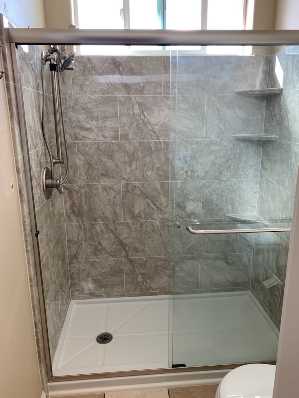 Remodeled walk-in shower with gray marble-look walls and stainless steel grab bar