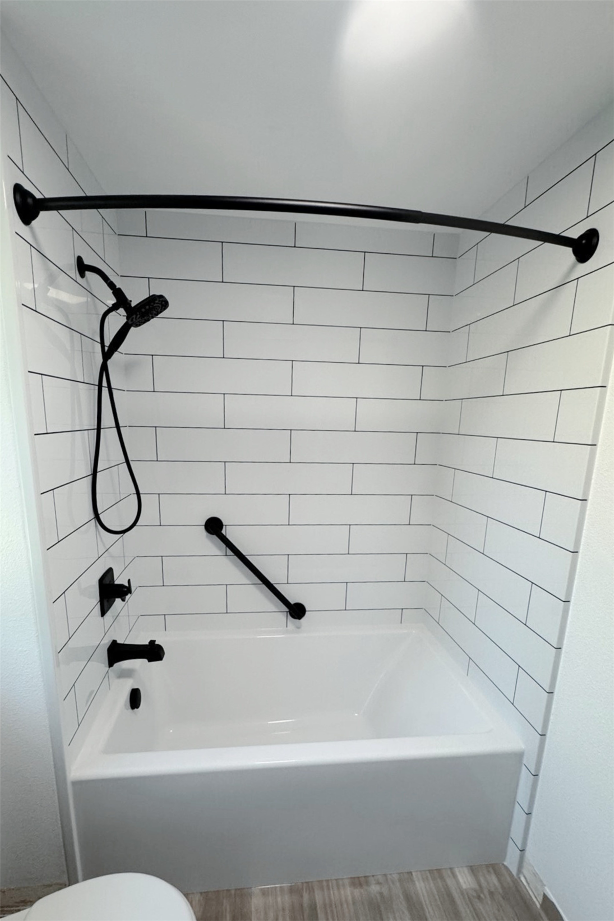 Replacement bathtub with white subway tile surround and black safety grab bar