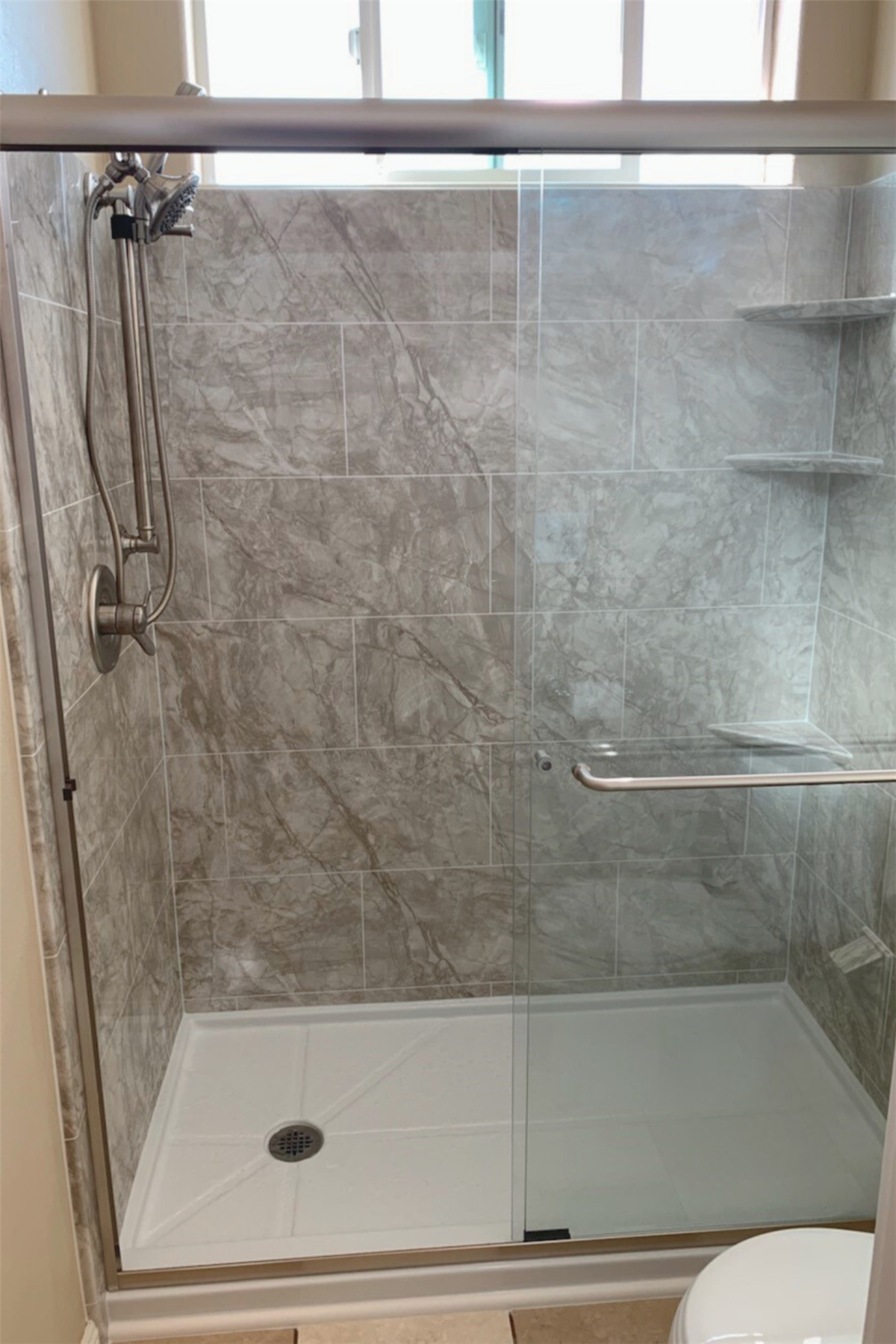 Walk-in shower with gray marble-look walls, glass enclosure, and stainless steel grab bar