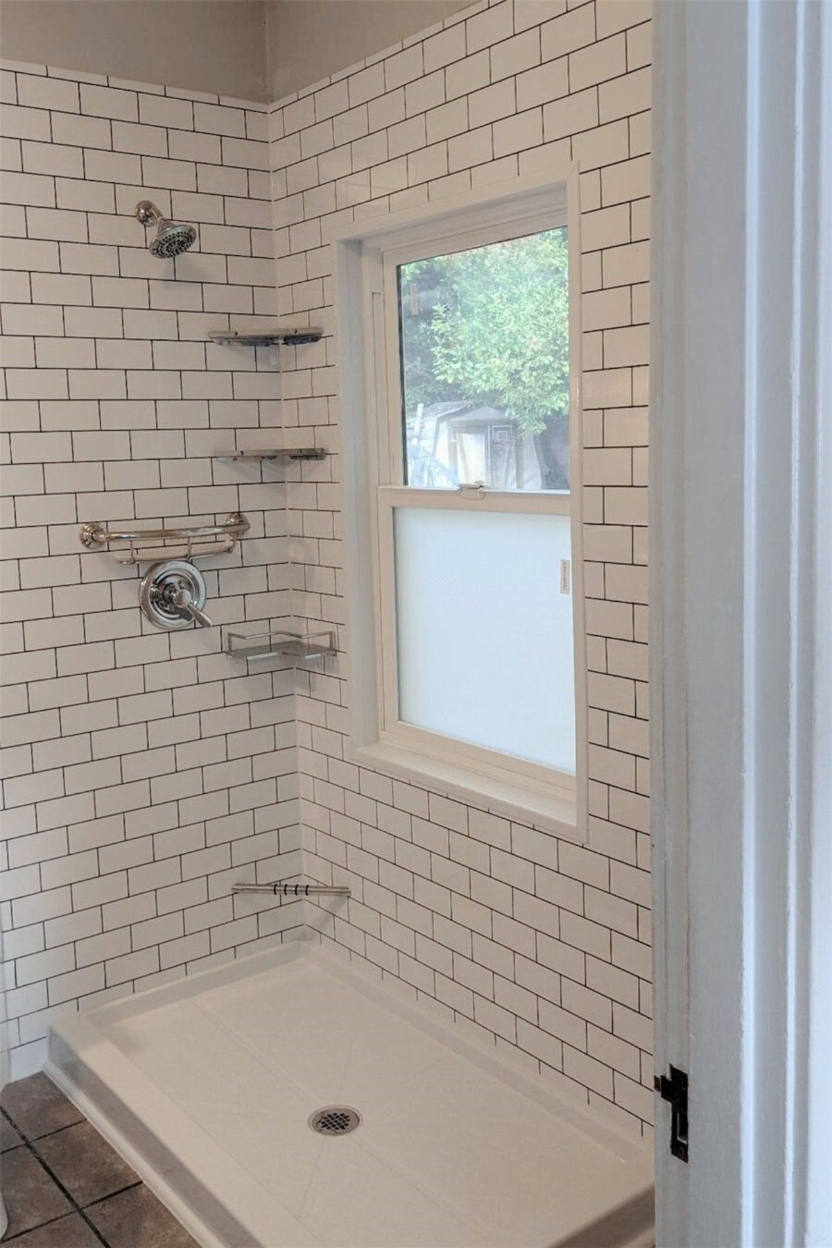 Walk-in shower with white subway tile walls and frosted bathroom window
