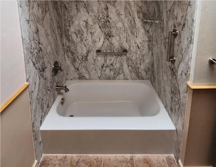 White bathtub with gray marble-look wall surround and built-in shelf