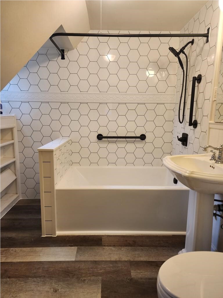 White bathtub with hexagon tile wall surround and black grab bar