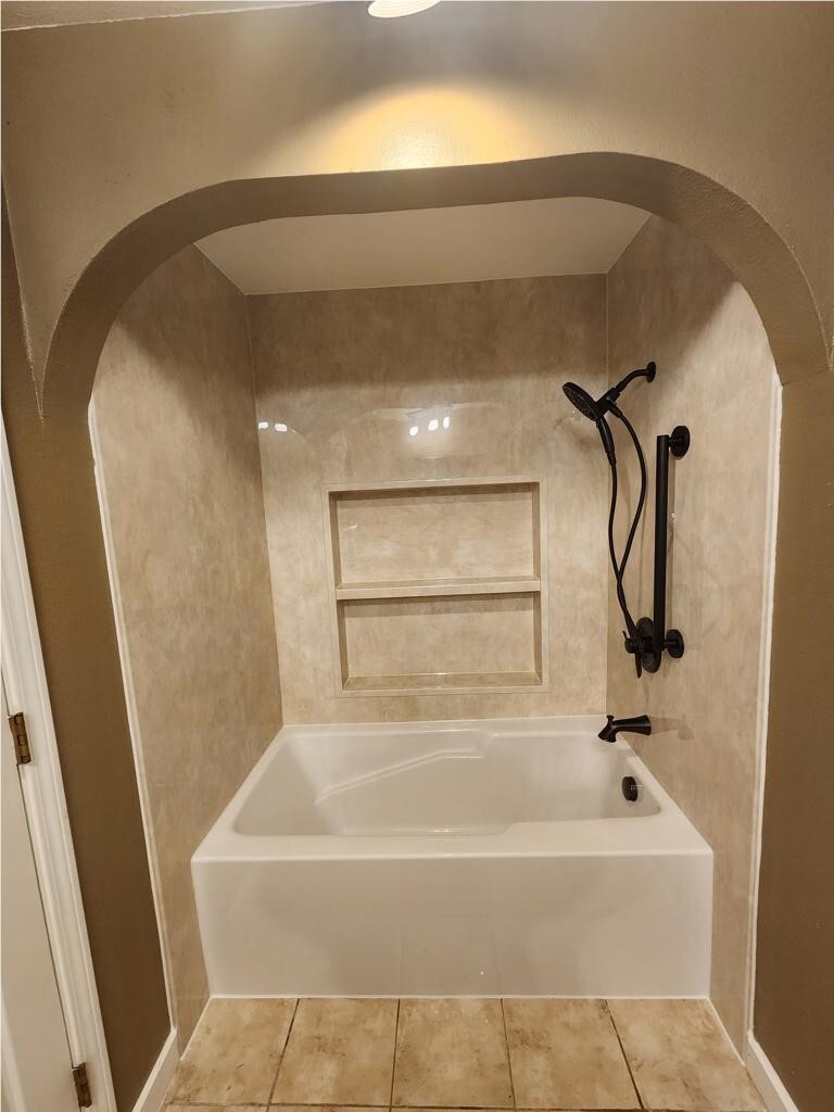 White bathtub with stone-look wall panels, recessed shelves, and black fixtures