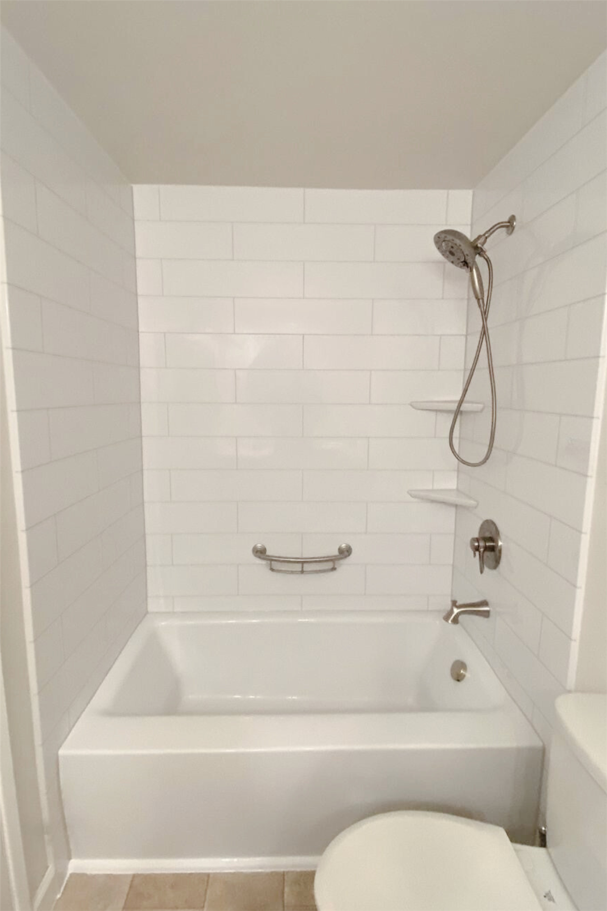 White bathtub with subway tile surround and stainless steel grab bar