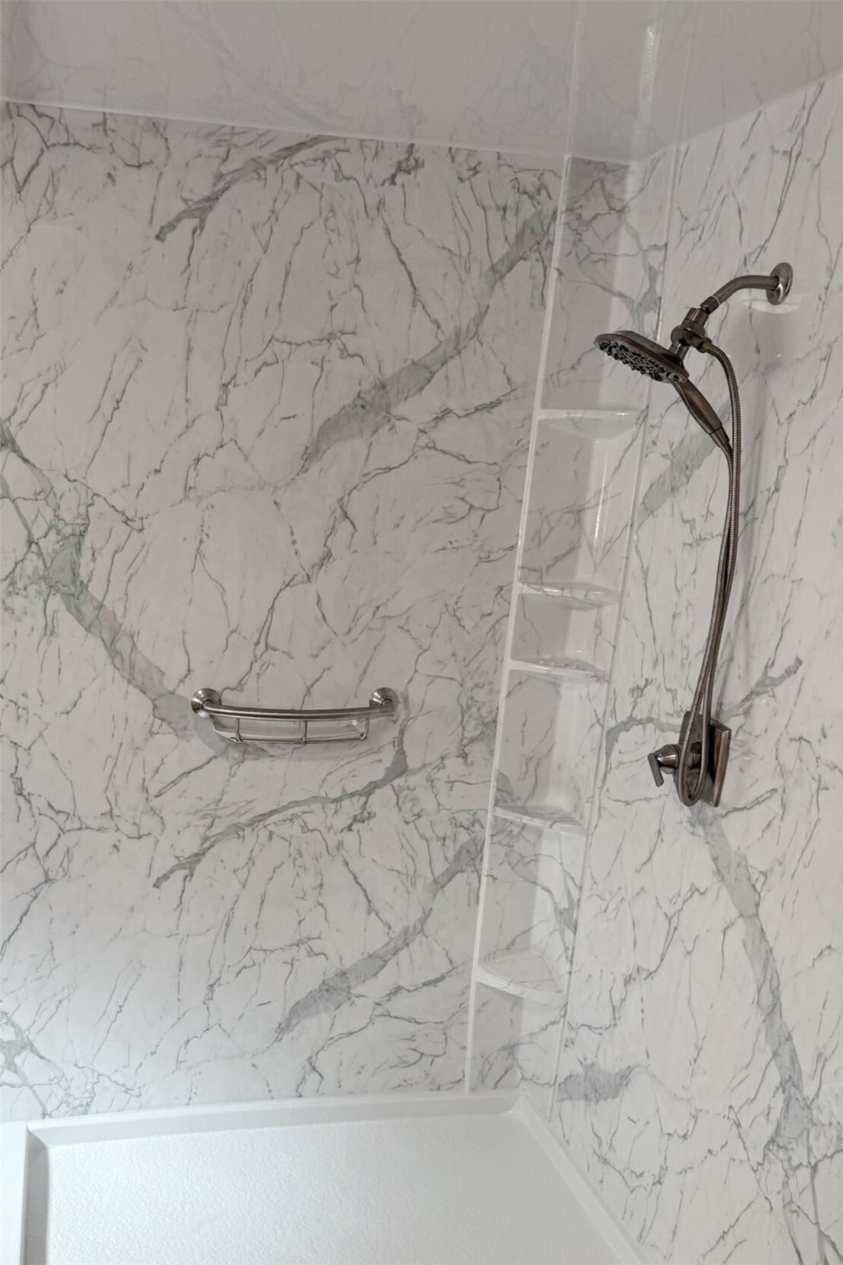 White marble-look shower wall with built-in corner shelves and grab bar