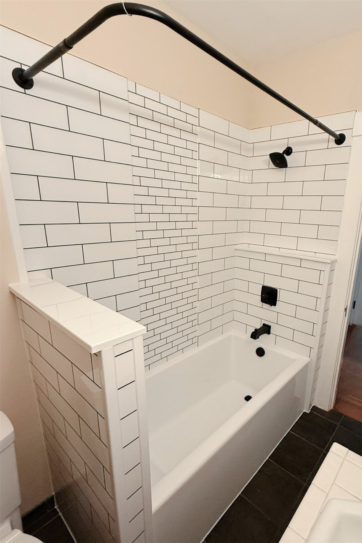 White subway tile bath wall surround with built-in corner ledge and black fixtures