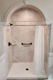 Light stone-look shower surround with built-in corner shelf and black safety grab bar