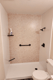 Light stone-look shower wall with black horizontal grab bar