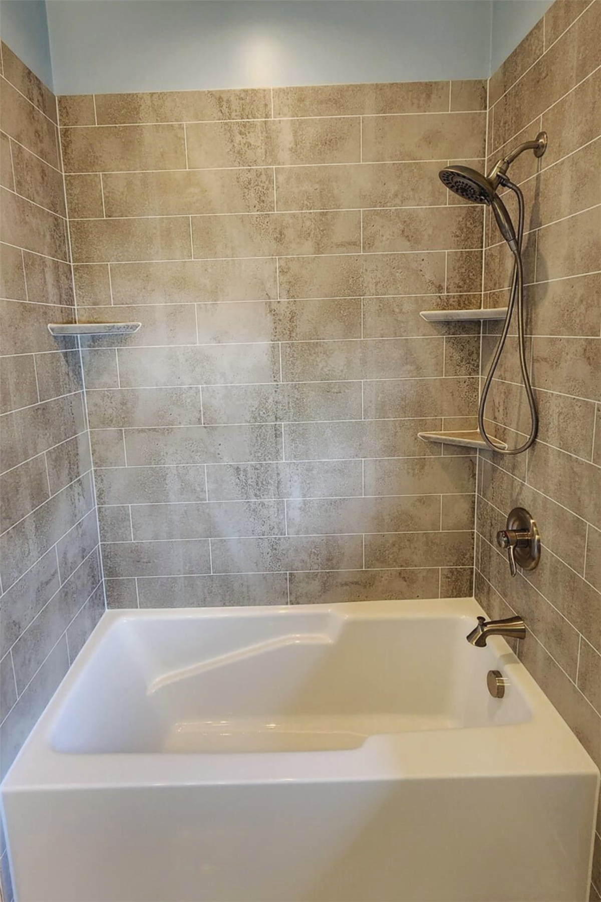 Shower-to-tub conversion with gray tile-look walls and built-in corner shelves