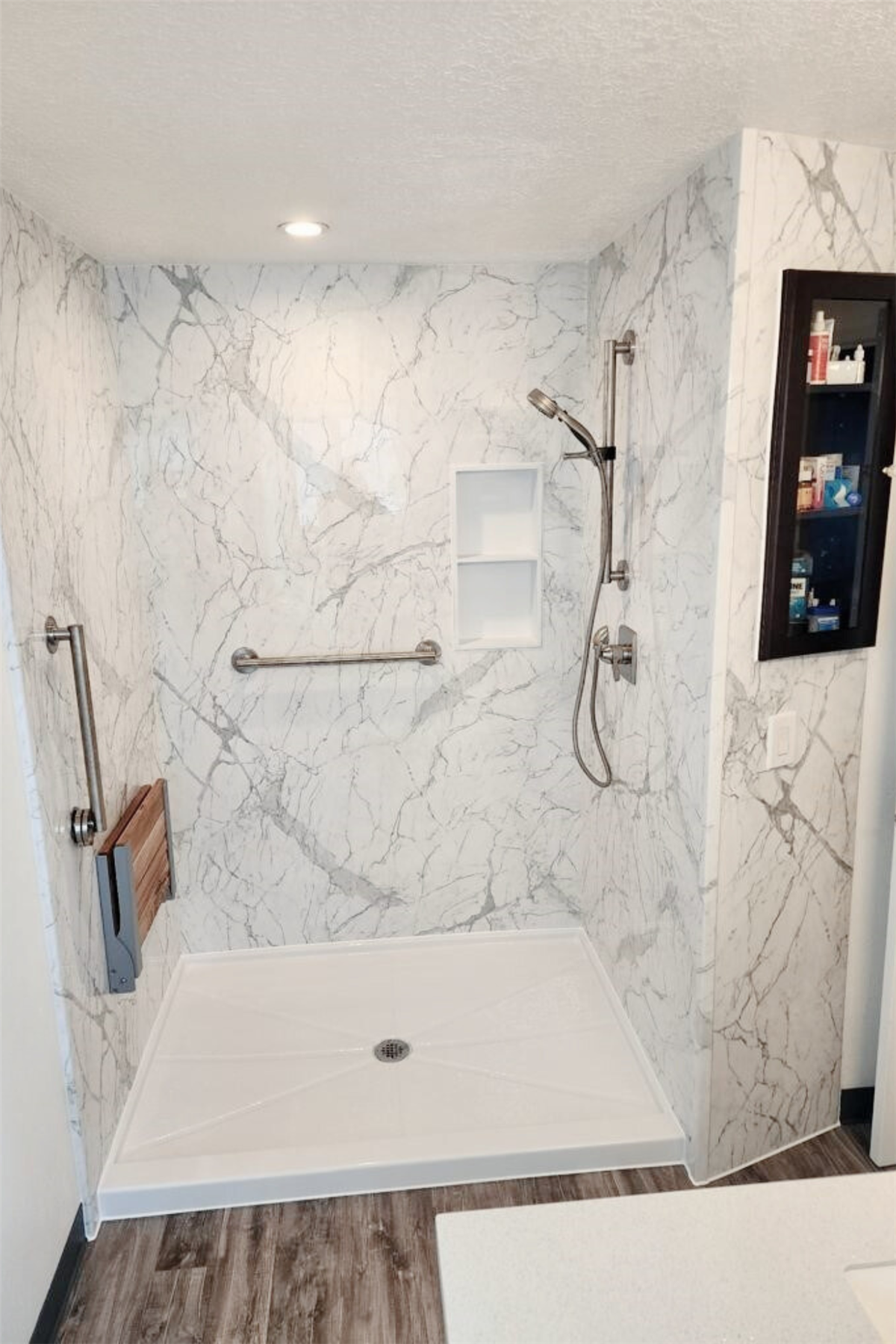 Tub-to-shower conversion with marble-look walls, recessed niche, handheld showerhead, and grab bar