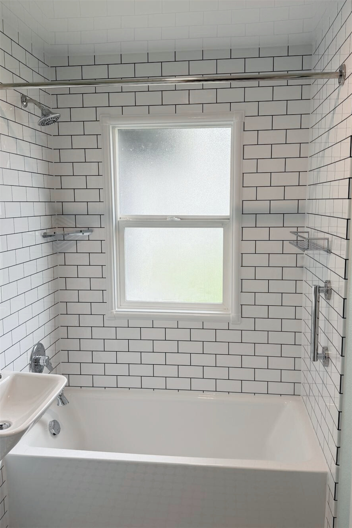 White subway tile bathtub surround installed around a frosted bathroom window