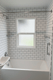 White subway tile bathtub surround installed around a frosted bathroom window
