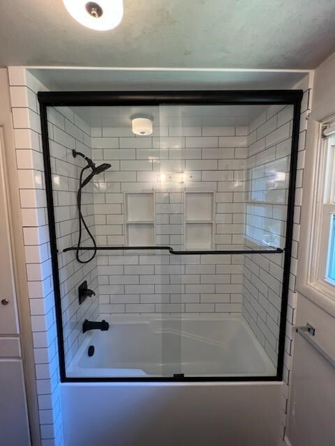 White subway tile shower with recessed niche, handheld showerhead, and black grab bars